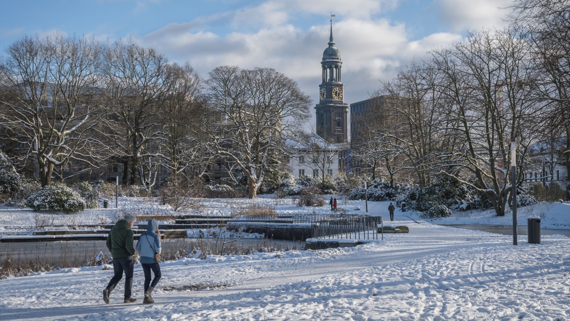 Zwei Spaziergänger laufen durch den mit Schnee bedeckten Park